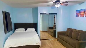 Un dormitorio con cama, ventilador de techo, suelo de madera, sofá y espejo.
