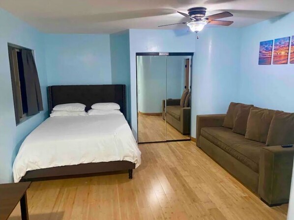 Un dormitorio con cama, ventilador de techo, suelo de madera, sofá y espejo.