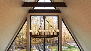 Um quarto com teto inclinado, uma janela ampla com vista para uma floresta e um candelabro.