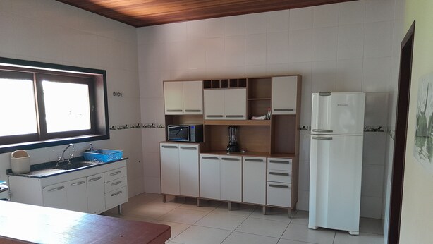 A compact kitchen with white cabinets, a built-in microwave, a coffee maker, and a refrigerator. - Residencial Seestern - Ancora (Cananéia)