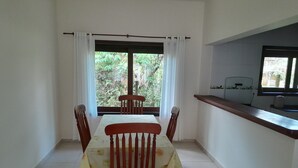 A dining area with a table and chairs, a window with curtains, and a kitchen counter. - Residencial Seestern - Ancora (Cananéia)