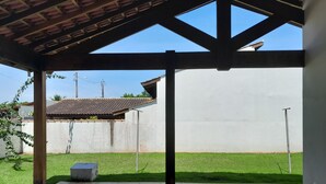 A covered patio area with a tiled floor, a concrete wall, and a view of a house with a tiled roof. - Residencial Seestern - Ancora (Cananéia)
