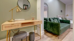 Un dormitorio moderno con escritorio, un sofá de terciopelo verde, un espejo redondo y una lámpara de noche.