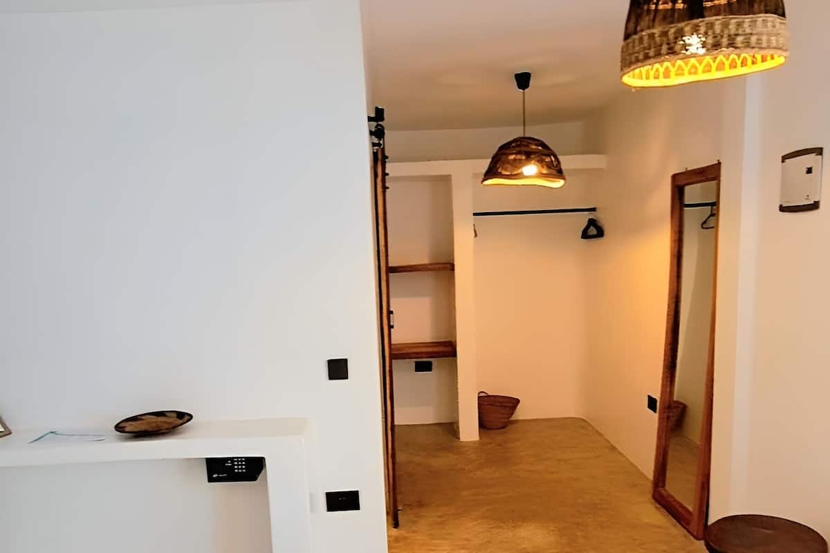A hotel room with a bed, a desk, a chair, a hanging light fixture, and a mirror.