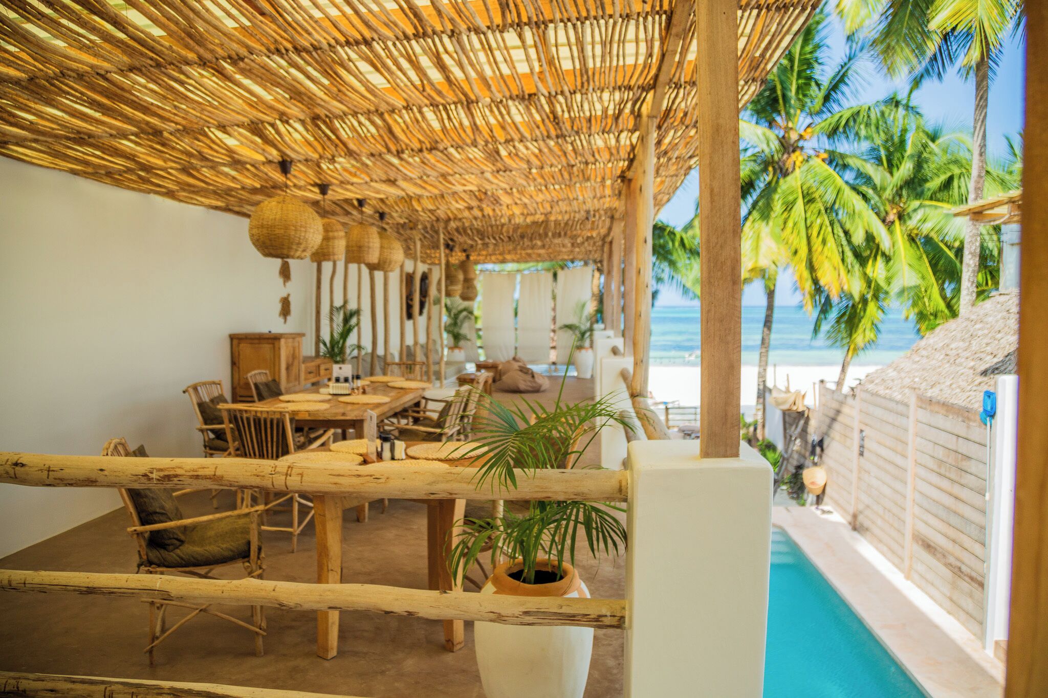 A beachside lounge with a thatched roof, wooden furniture, and a view of the ocean.