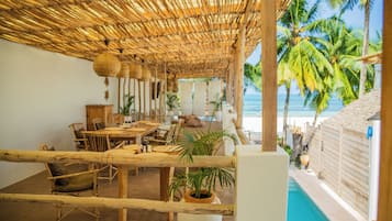 A beachside lounge with a thatched roof, wooden furniture, and a view of the ocean.