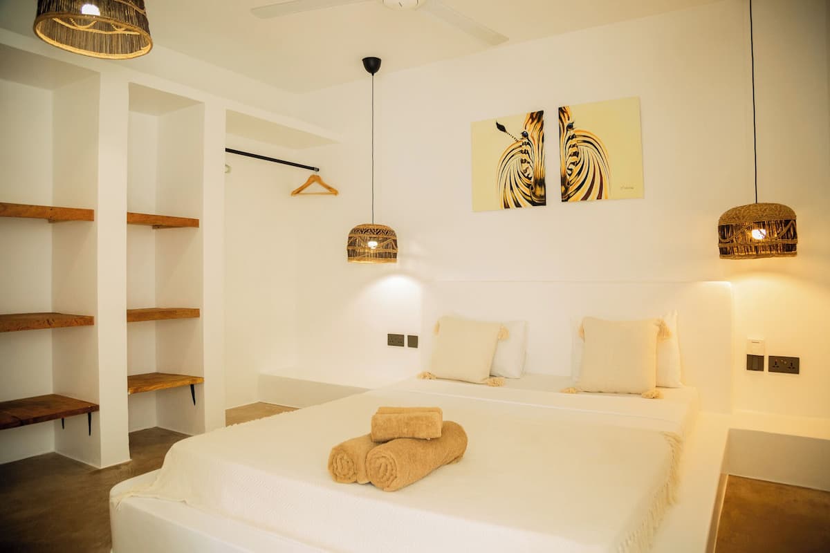 A hotel room with a large bed, wooden shelves, a hanging light fixture, and a wall art piece.