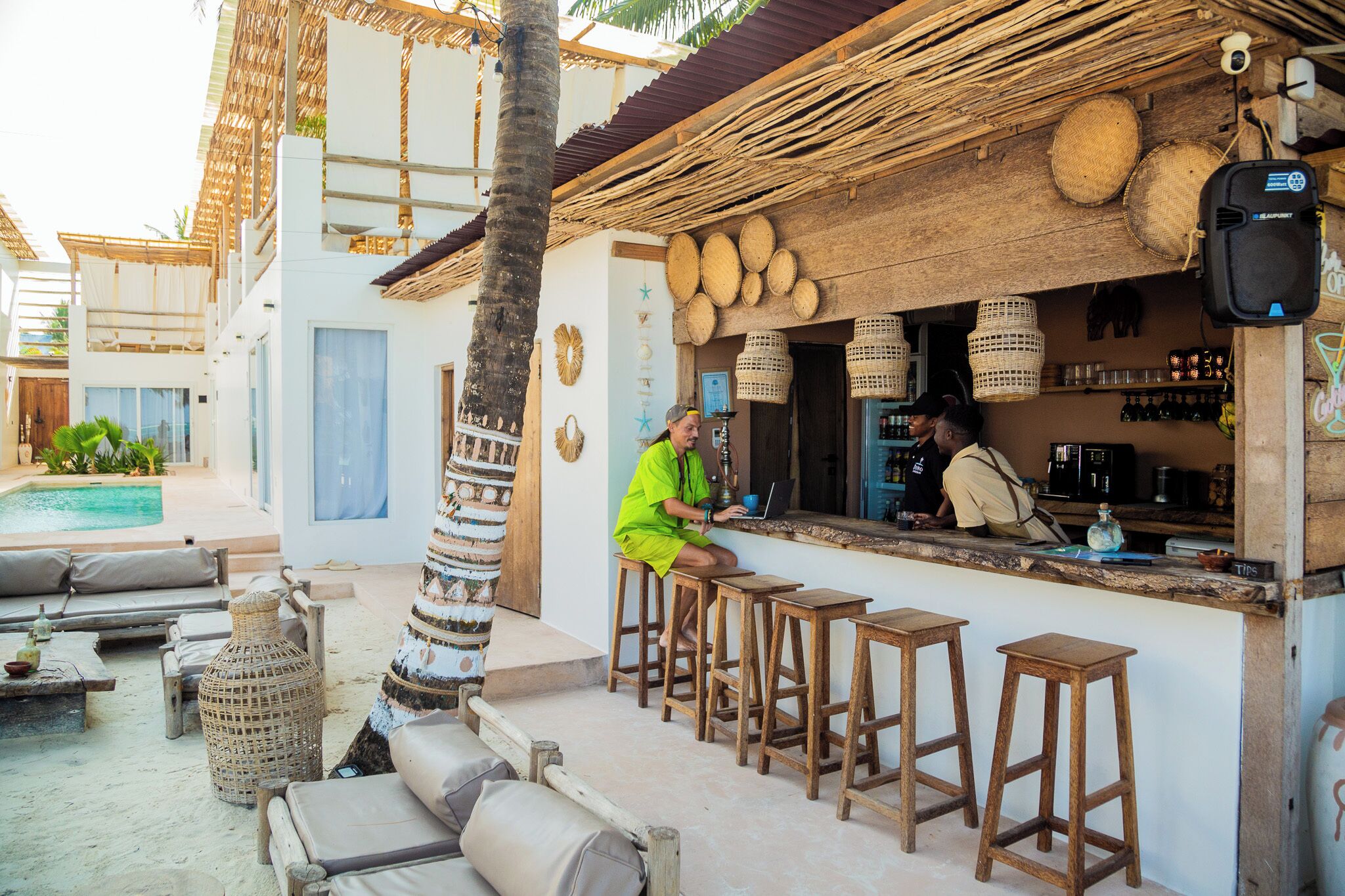 A bar area with wooden stools, a pool, and a tropical setting.