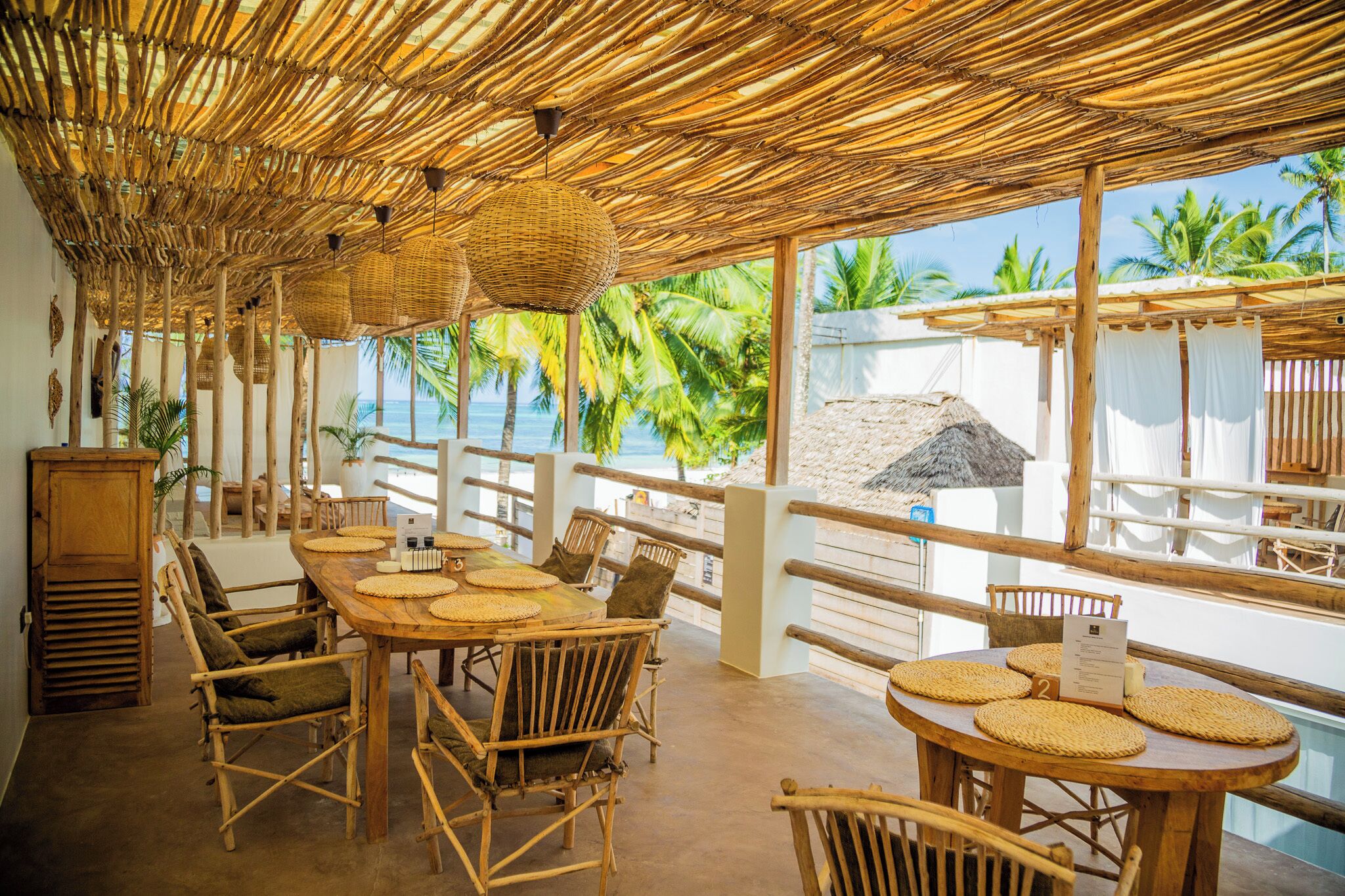 Un restaurante frente a la playa con techos de bambú, mobiliario de mimbre y vista al océano.