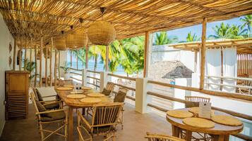 Un restaurante frente a la playa con techos de bambú, mobiliario de mimbre y vista al océano.