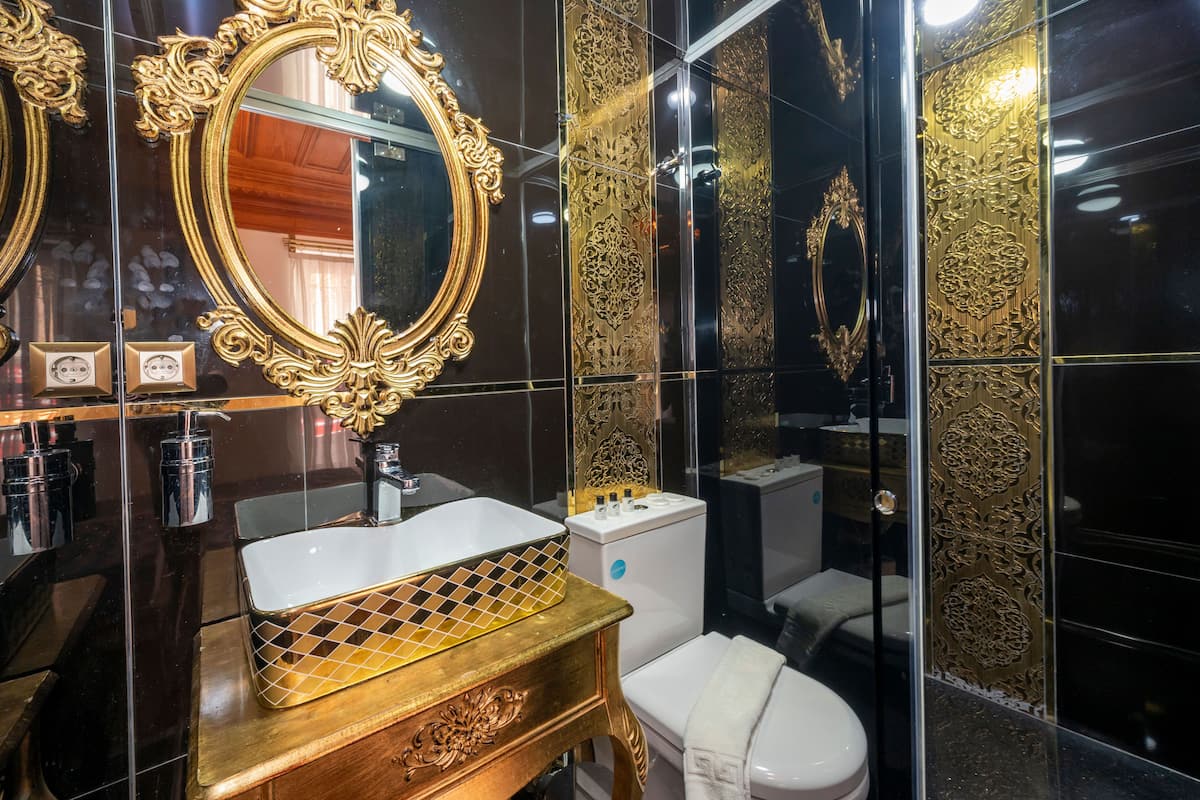 A bathroom with a gold-framed mirror, a white sink, and a toilet.