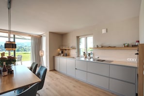 Eine moderne Küche mit Essbereich, großen Fenstern und Blick ins Freie.