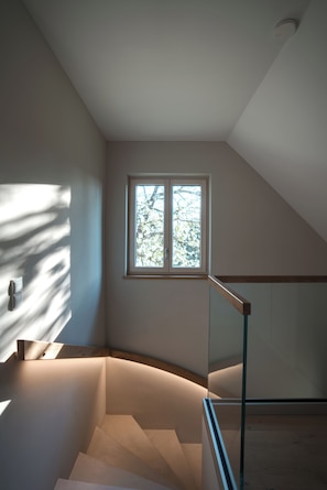 Eine moderne Treppe mit Glasgeländern, ein Fenster mit Blick auf Bäume und eine Deckenleuchte.