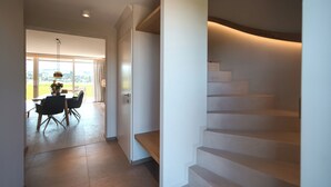 Un interno moderno con una scala, una zona pranzo con sedie e tavolo, e una vista attraverso un'ampia finestra.