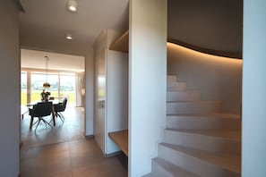 Ein modernes Interieur mit einer Treppe, einem Essbereich mit Stühlen und einem Tisch sowie einem Ausblick durch ein großes Fenster.