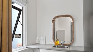 A modern kitchen with white cabinets, a stainless steel sink, and a large mirror with a woven frame.