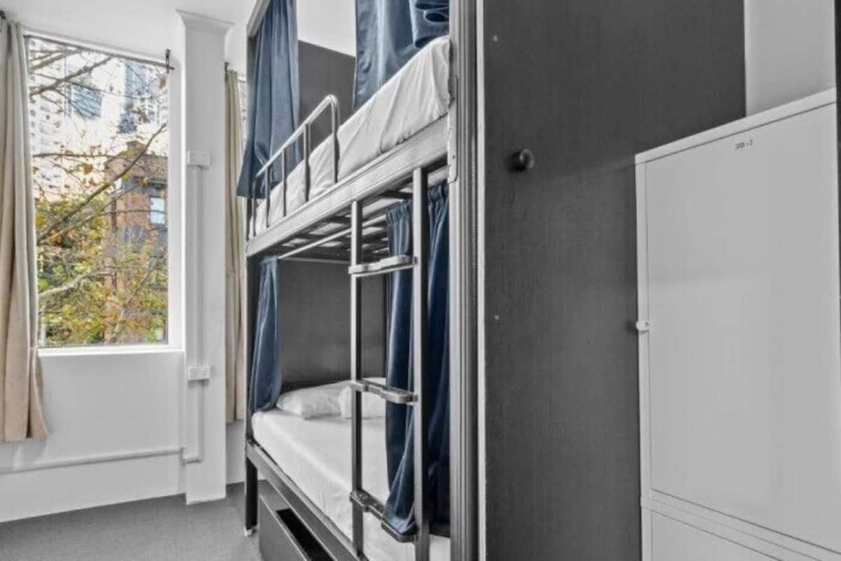 A bunk bed room with a window, curtains, and a white wardrobe.