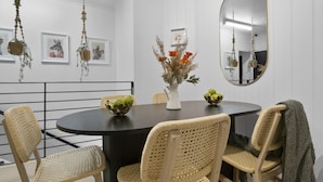 A dining area with a round table, wicker chairs, a vase with flowers, and framed pictures on the wall.