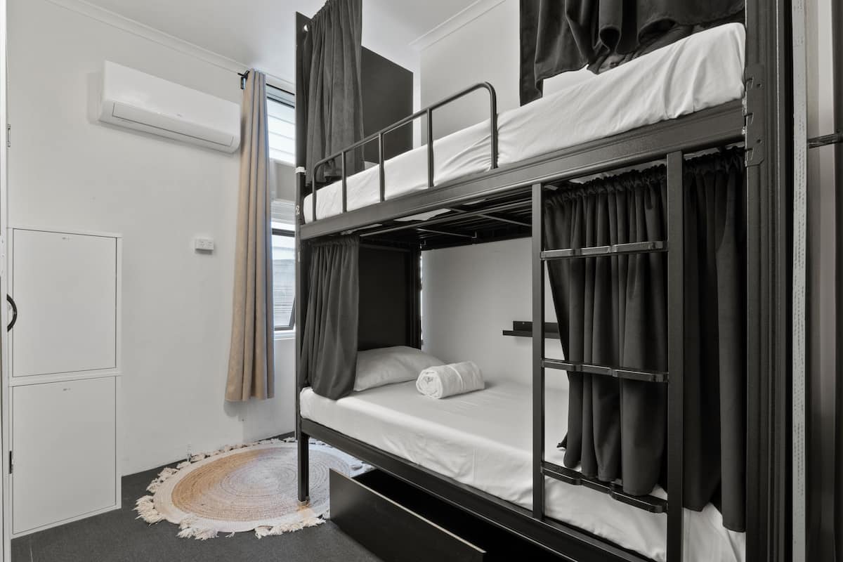 Habitación con literas, una puerta blanca, un tapete redondo pequeño y una cortina.