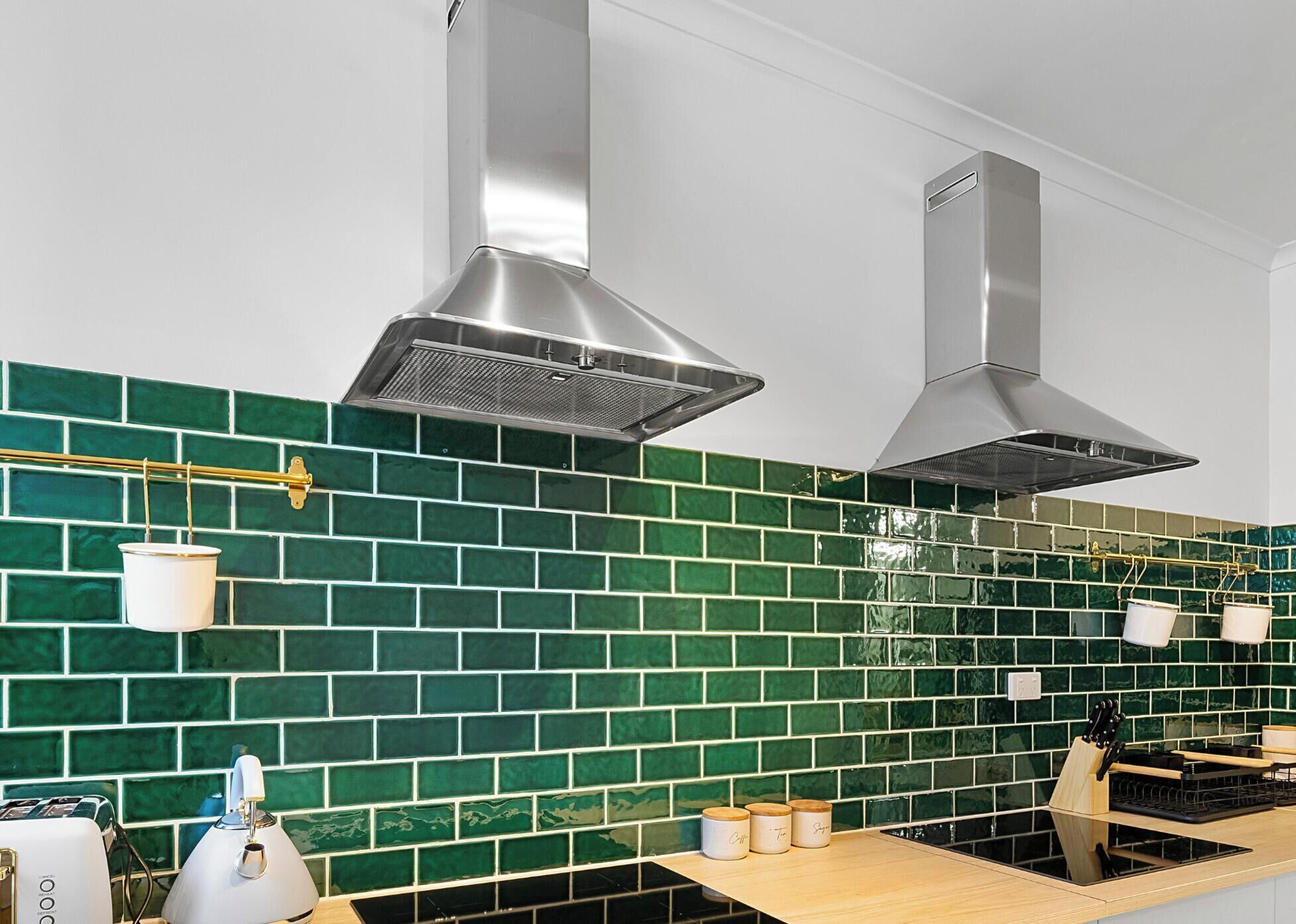 A kitchen with green tiled backsplash, stainless steel range hood, and a wooden countertop with a toaster and knife block.