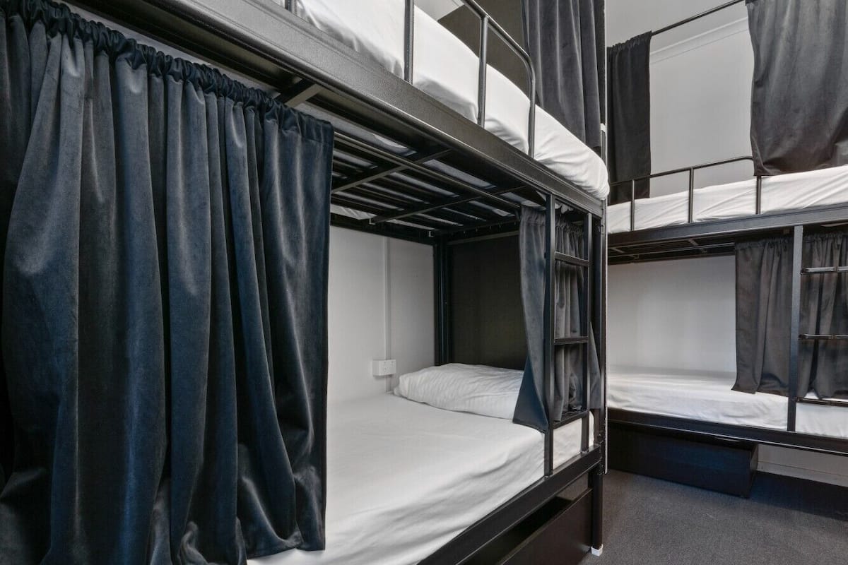 A bunk bed room with curtains, a window, and a wall socket.