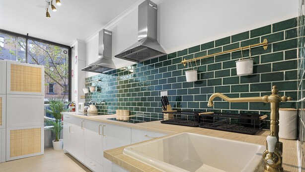 A modern kitchen with white cabinets, a large sink, and a green-tiled backsplash.