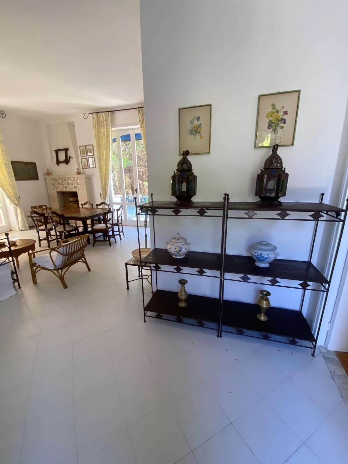 Un comedor con una mesa redonda y sillas, una chimenea y una estantería decorativa con objetos.