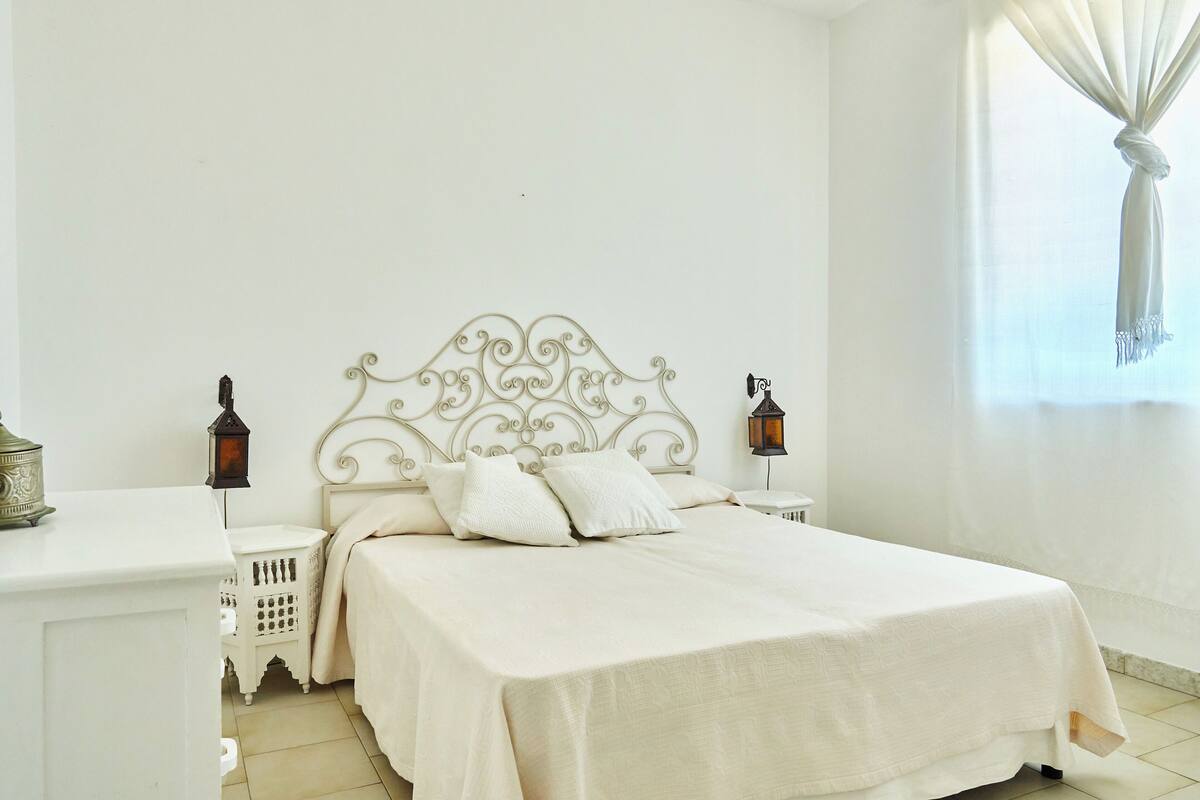 A bedroom with a white bed, white nightstands, and a decorative headboard.