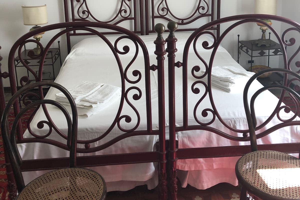 A bedroom with a double bed, two chairs, a nightstand, and a painting on the wall.