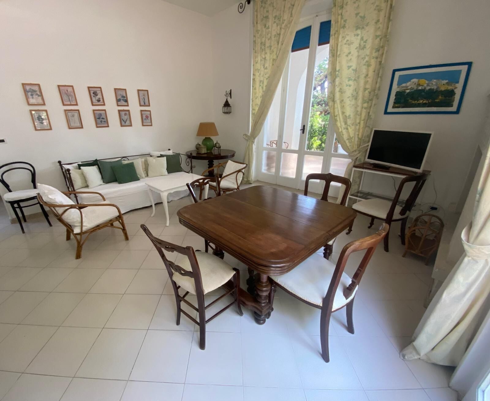 A dining area with a wooden table and chairs, a sofa, and a television.