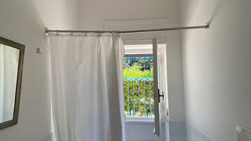 Un baño con bañera, cortina de ducha, toalla y ventana con vistas a follaje.