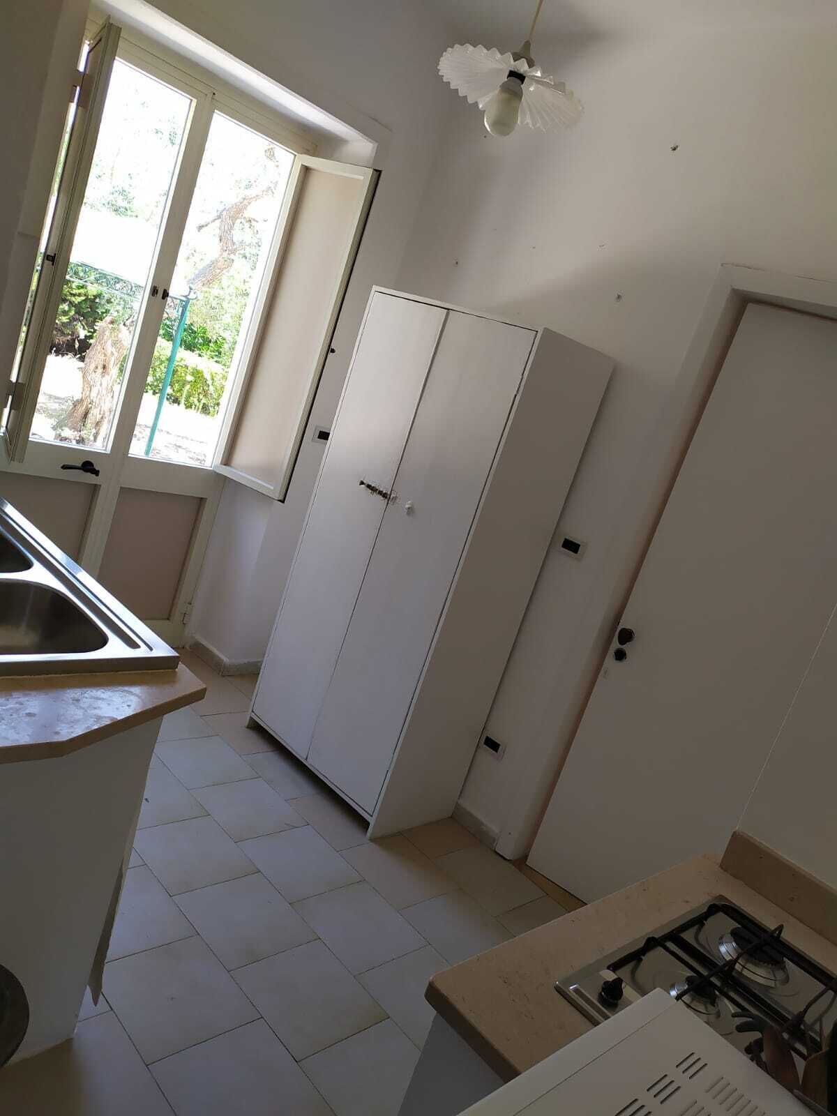 Una cocina con estufa a gas, lavamanos, armario y ventana con vistas al verdor.