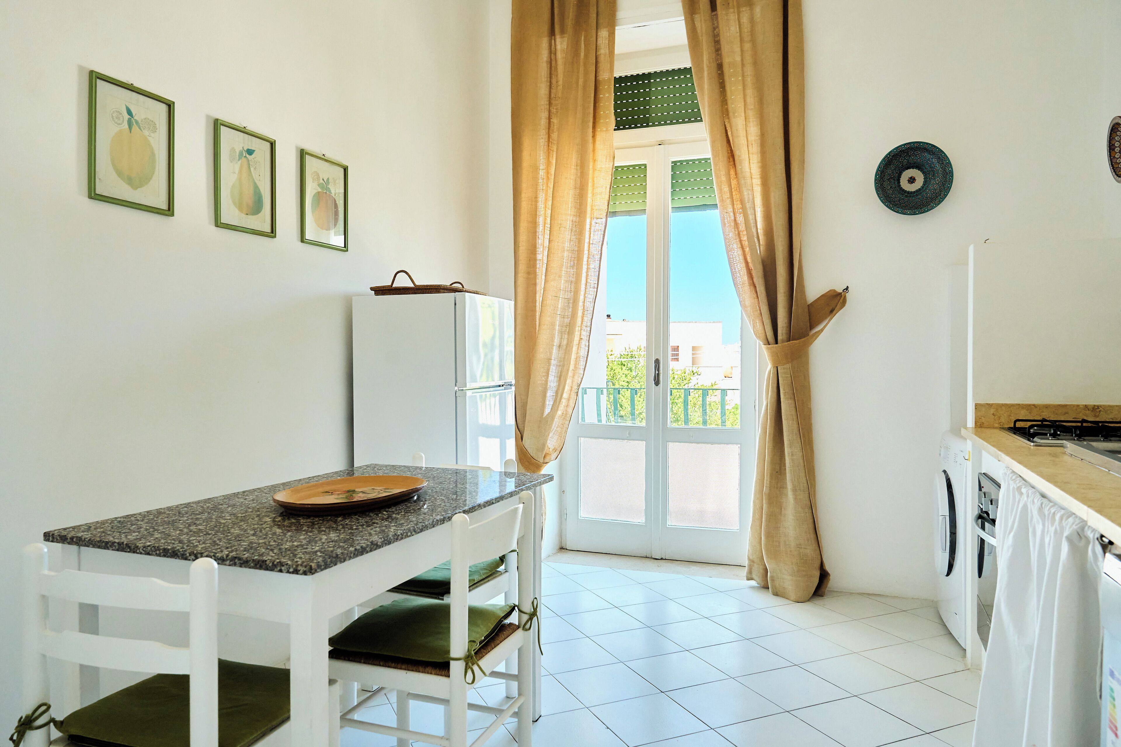 A small kitchen with a dining table, chairs, a washing machine, and a window with curtains.