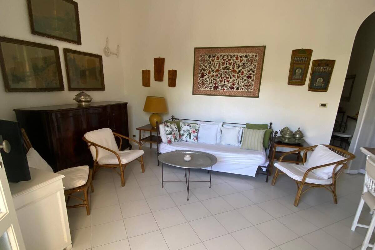 A living room with a sofa, two armchairs, a coffee table, and a TV. There are framed pictures on the wall and a lamp on a side table.