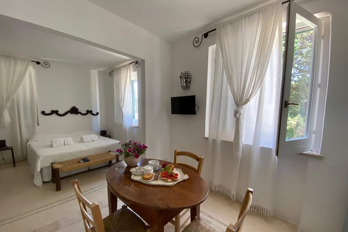 A bedroom with a bed, a bedside table, a TV, and a window with curtains.