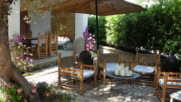 An outdoor seating area with wooden furniture, a woven umbrella, and a stone table with candles.