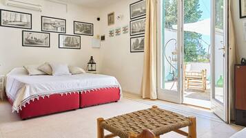 A bedroom with a bed, a red bench, and a balcony with a view of the outdoors.