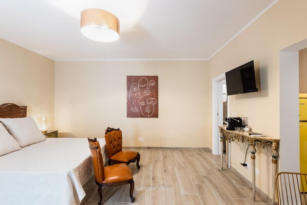 A bedroom with a bed, two chairs, a coffee machine, and a TV on the wall. - Bowie's Rooms (Noto)