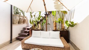 A cozy room with a wicker sofa, a large umbrella, and potted plants. - Bowie's Rooms (Noto)