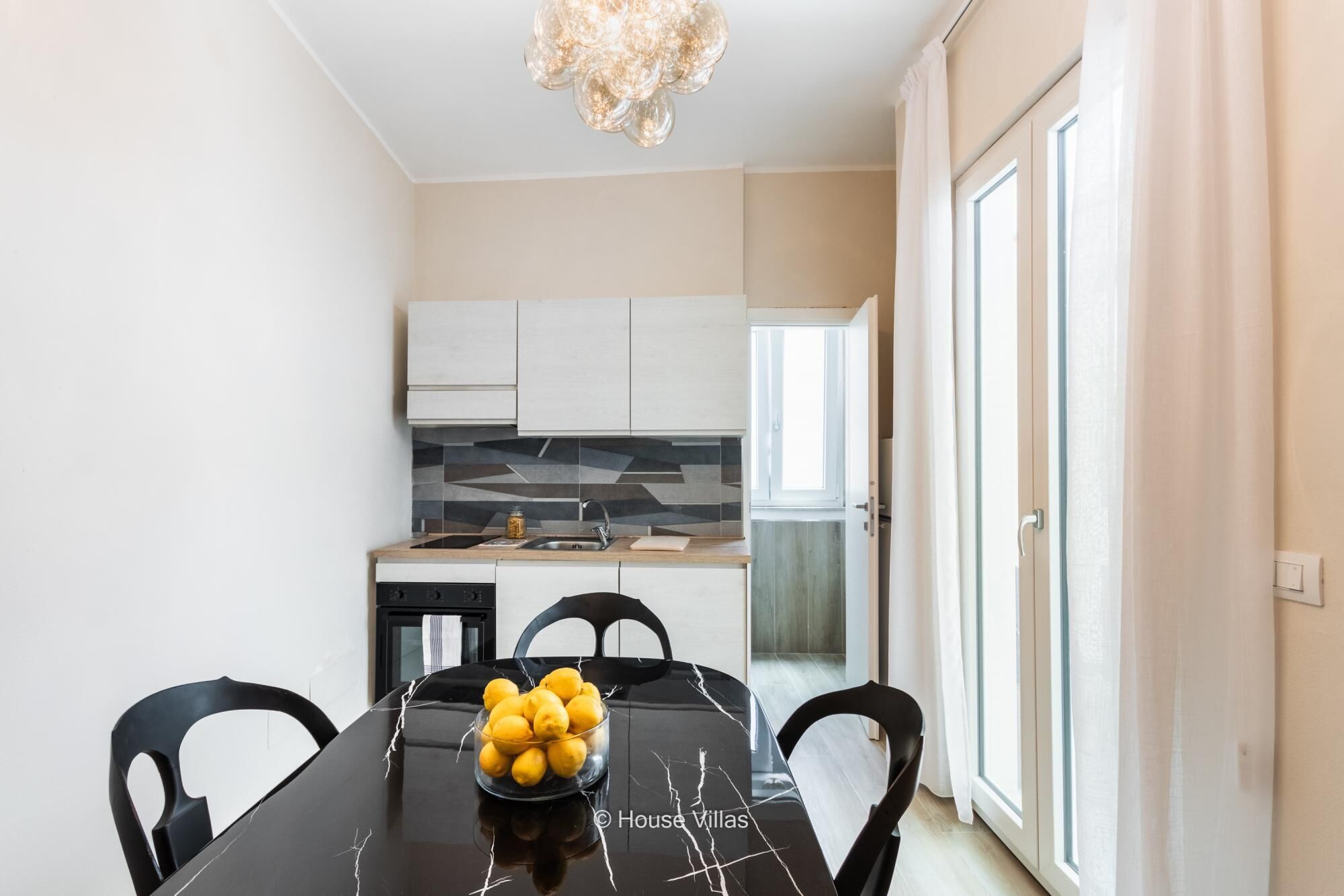 A modern kitchen with white cabinets, a marble countertop, and a dining table with chairs.