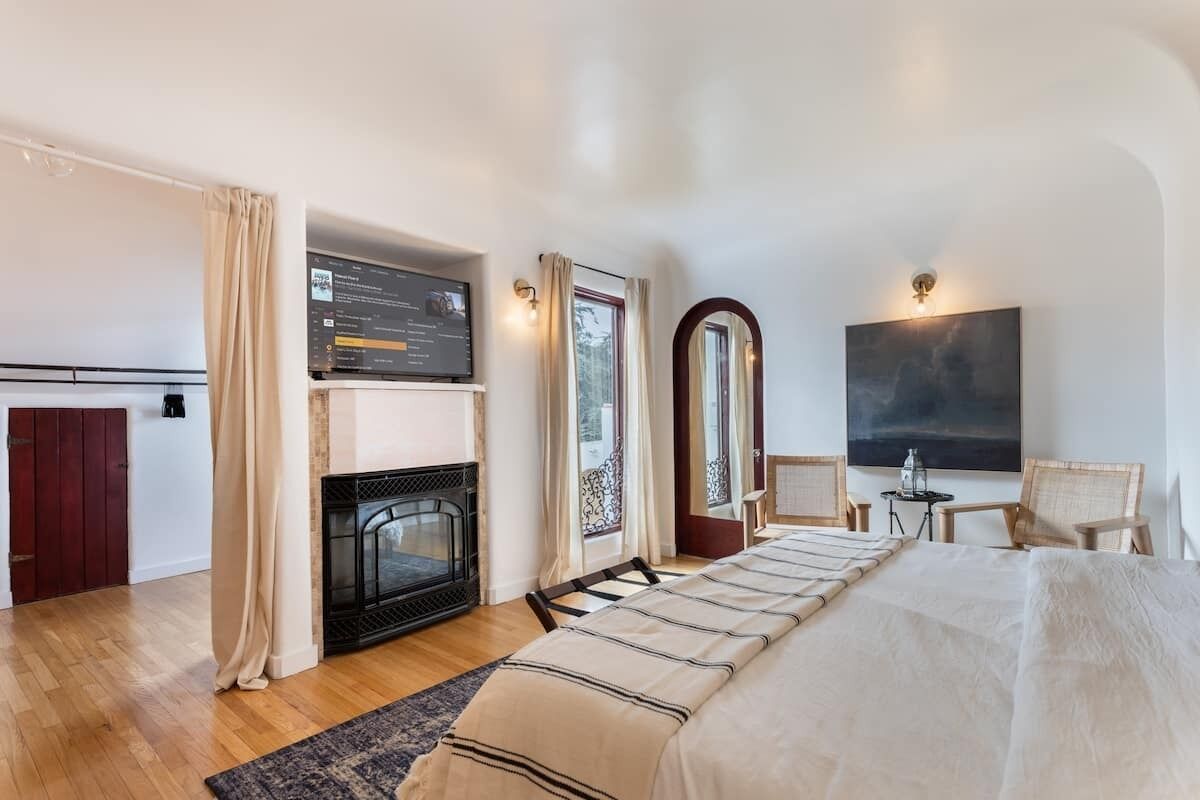 A modern hotel room with a fireplace, a bed with a striped bedspread, a large mirror, and a painting on the wall.