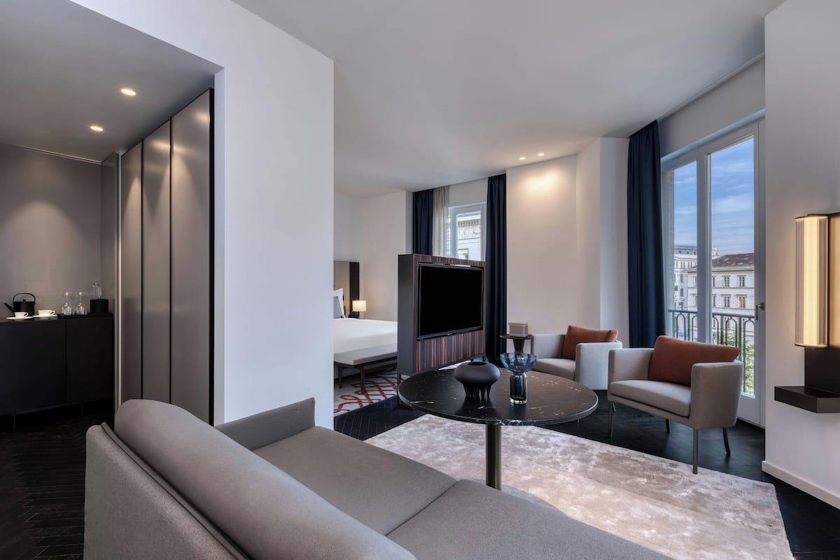 A modern hotel room with a sofa, a round coffee table, a bed, and a TV.