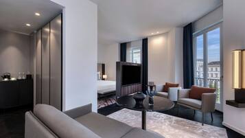 A modern hotel room with a sofa, a round coffee table, a bed, and a TV.