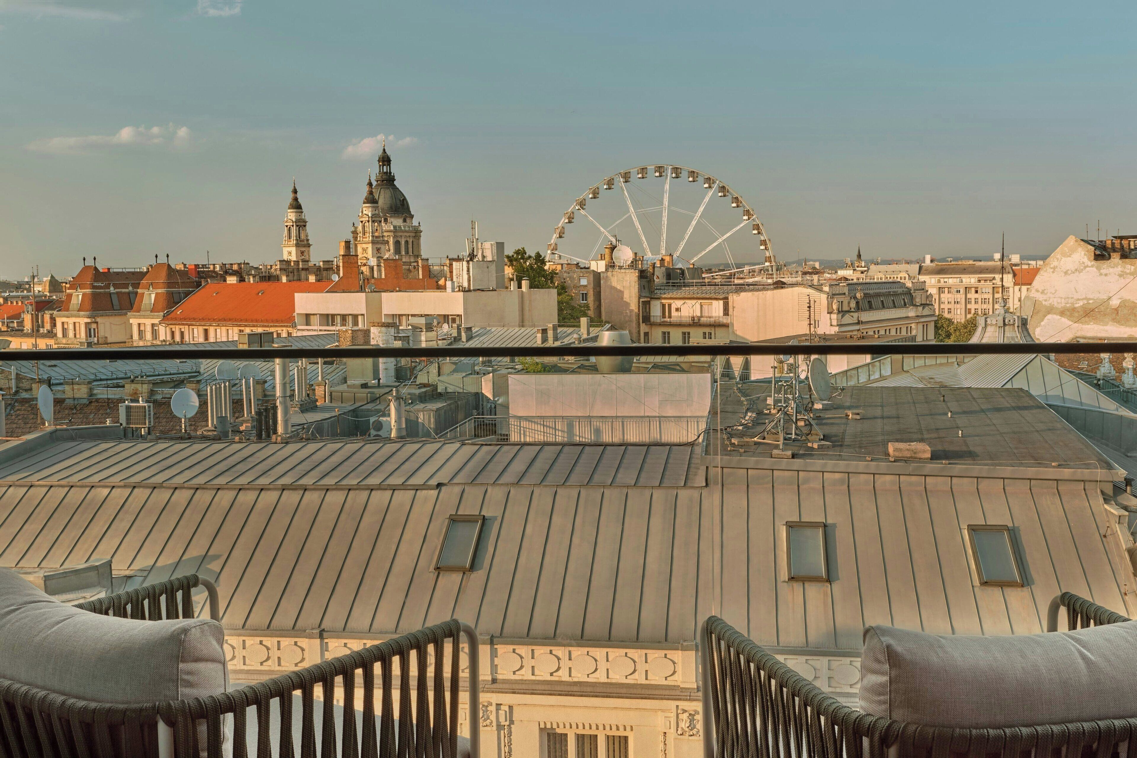 Terraza en la azotea con vistas a un paisaje urbano, incluyendo una noria grande y edificios históricos.