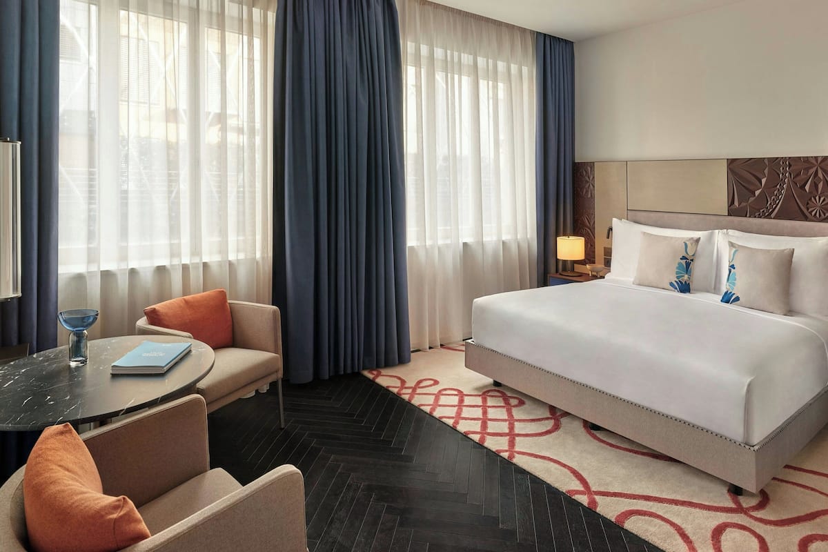 A hotel room with a bed, a sofa, a table with a book, and a lamp.
