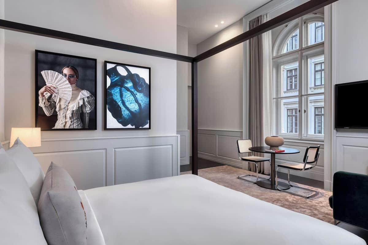 A hotel room with a large bed, a dining table with chairs, a television, and artwork on the walls.