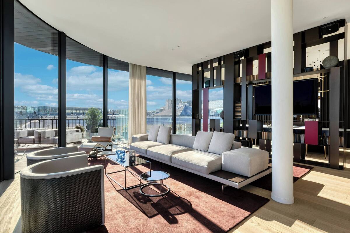 A modern living room with a white sofa, a glass coffee table, and a view of the city through large windows.