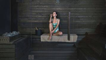 A person sitting on a bench in a sauna with a wooden wall and a stone bench.