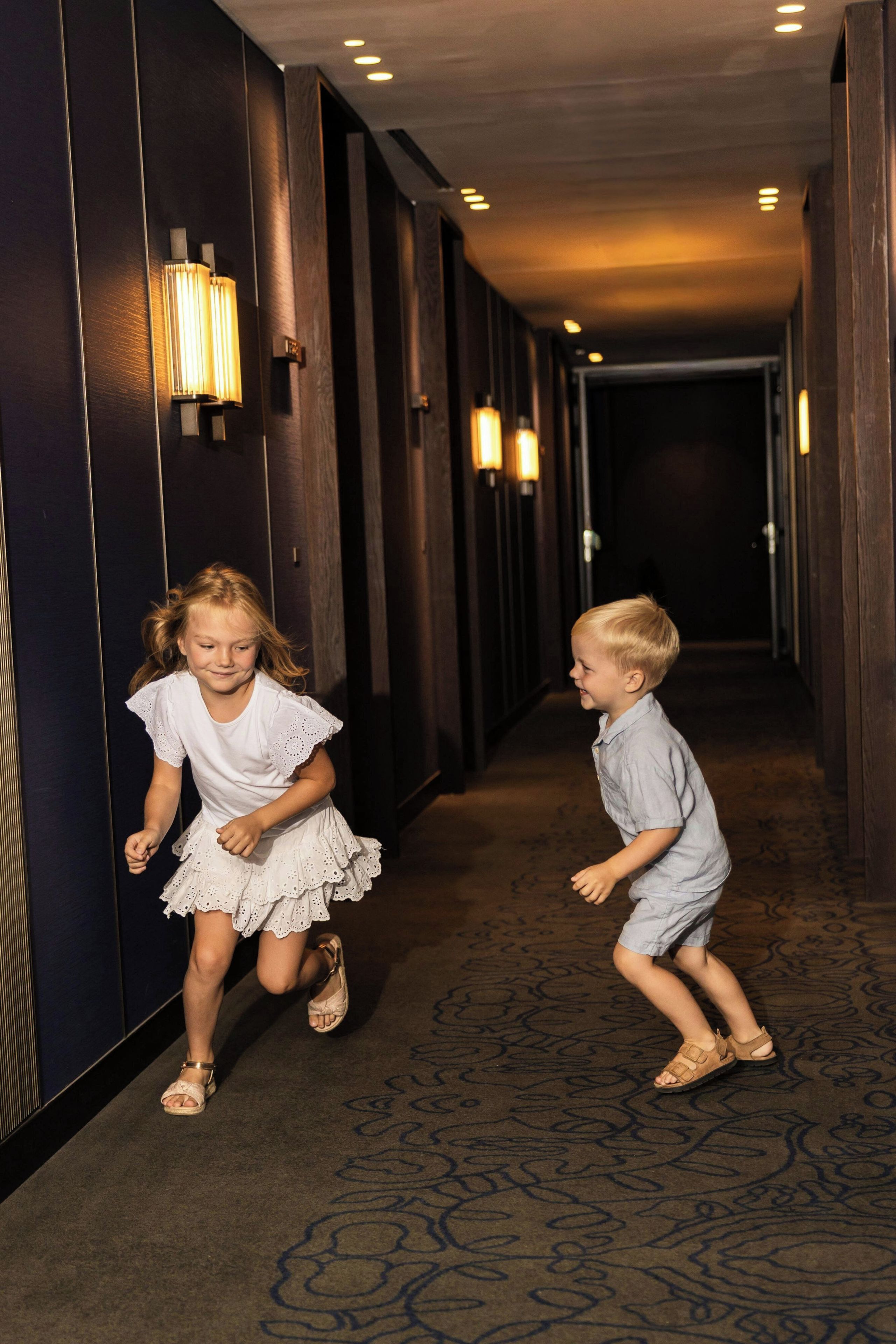 A hotel hallway with a carpeted floor and wall-mounted lighting.
