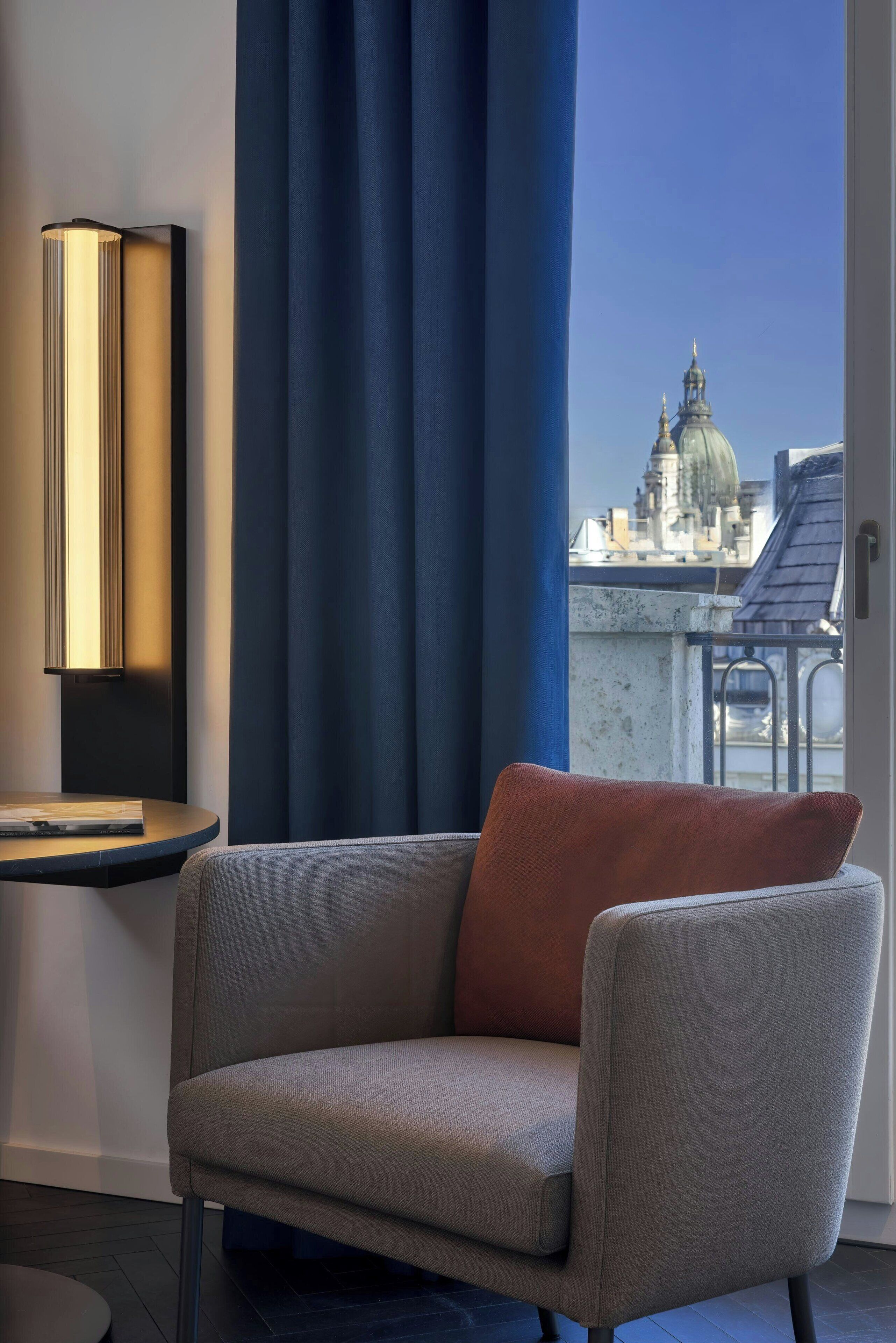 A modern room with a grey sofa, a blue curtain, and a view of a cityscape with a dome structure.
